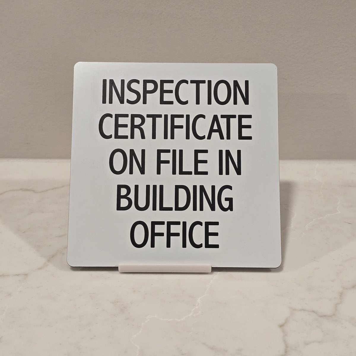 White engraved sign reading Inspection Certificate On File In Building Office