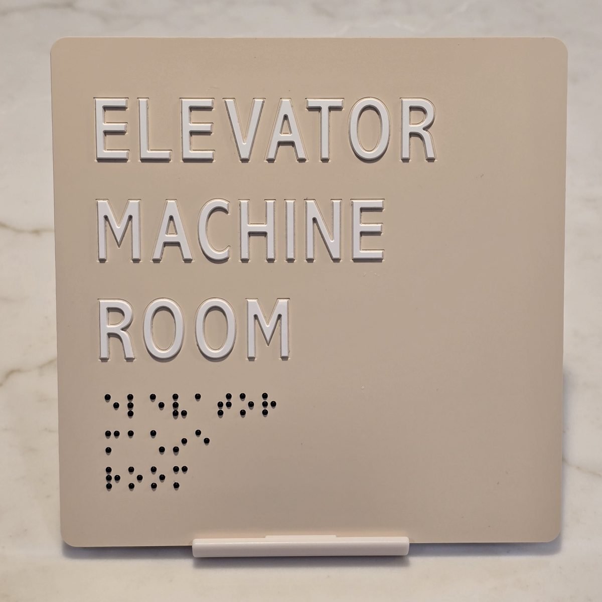 Almond ADA sign reading Elevator Machine Room with raised white characters and black raster braille