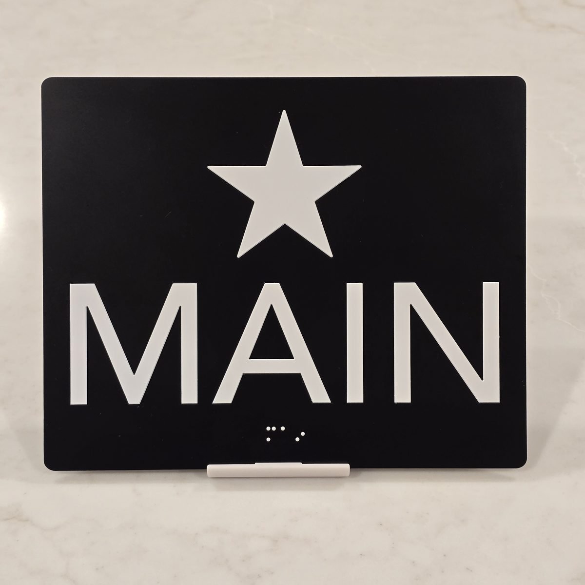 Black jamb plate with white star of main egress and the word MAIN with raster braille